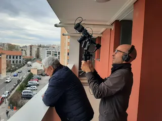 Élie est sur son balcon. Il regarde la rue tandis que Marc le film de dos