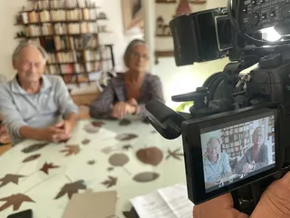 Bernard et Eliane sont assis dans leur cuisine. La caméra les filmant est en léger hors champ.