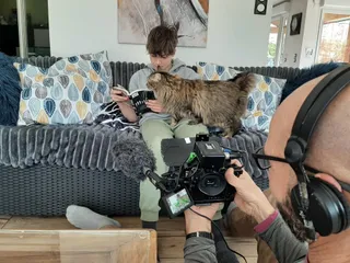 Marc film un ado chez lui. Ce dernier sweet gris et pantalon vert est sur son canapé gris, en train de lire. Sur lui un chat très curieux de cette lecture.