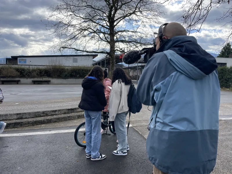 Marc filme deux collégiennes observant une troisième camarade faisant du vélo. Les deux collégiennes sont de dos. Elles portent leurs sacs à  dos à l'épaule et manteau pour se protéger du froid de l'hiver.