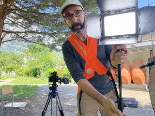 Marc, habillé d'un gilet fluo, règle une lumière de tournage. La lumière pointe vers la caméra.